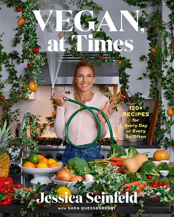 Vegan At Times cookbook cover shows Jessica Seinfeld holding a garden hose, surrounded by fruits and vegetables in a kitchen 